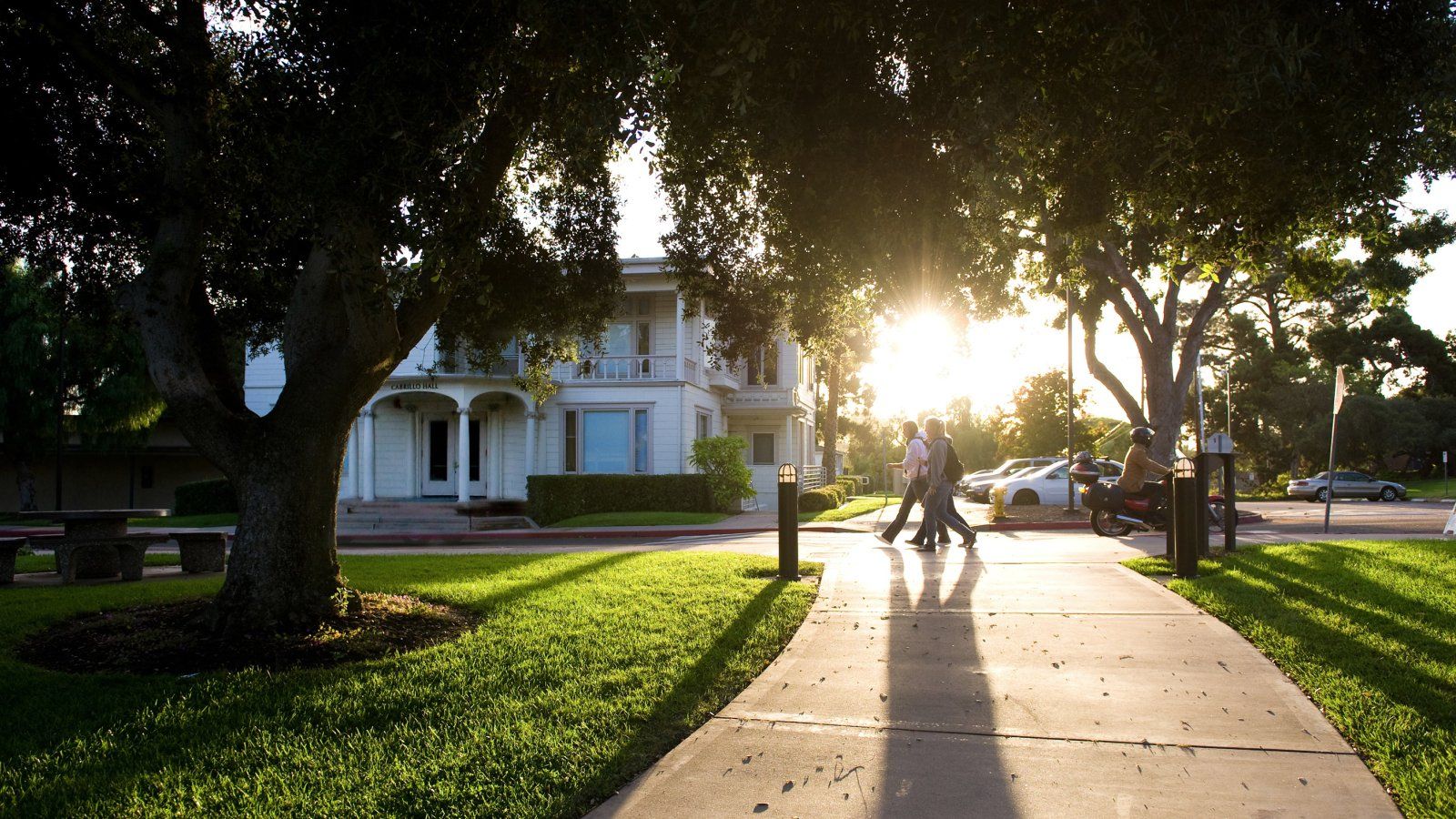 Students walk past Cabrillo Hall with the sun in the background.