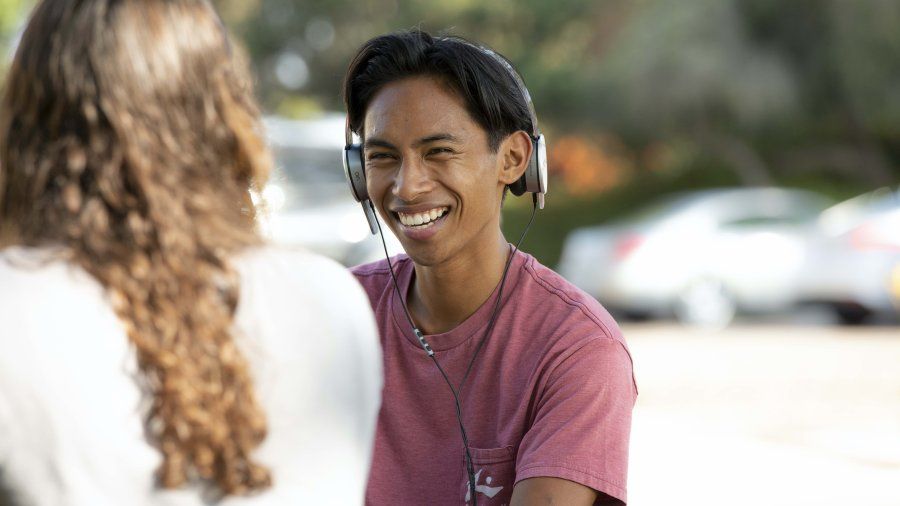Male student wearing headphones looks up and smiles from his laptop