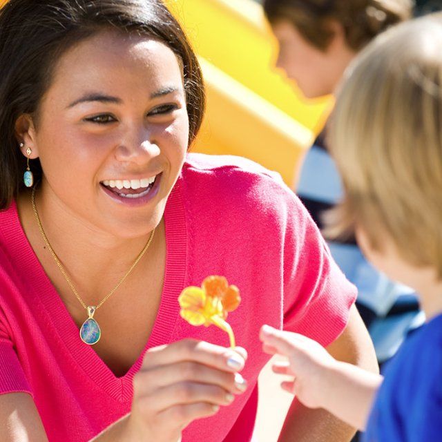 A female ECLC student worker hands a small orange flower to a child in the playground