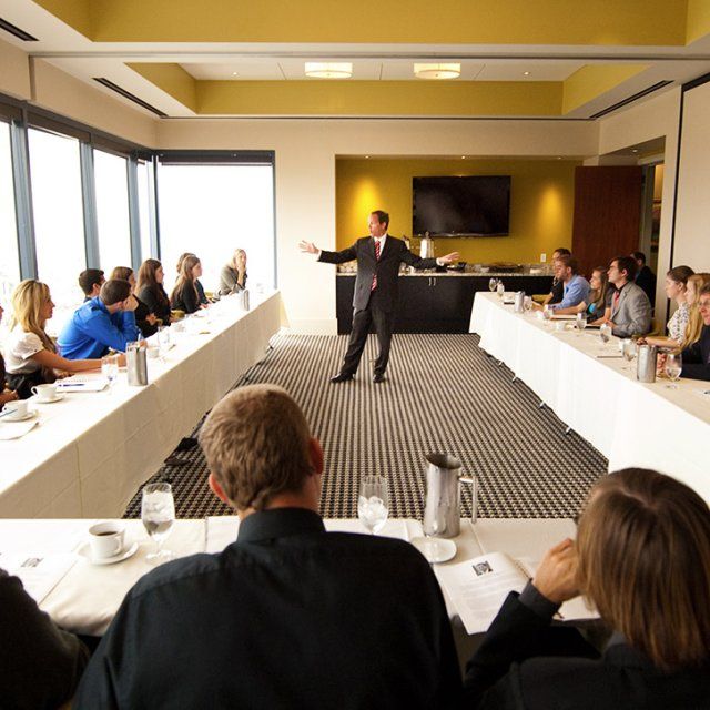 A speaker in a business suit presents in a conference room during a breakfast event.