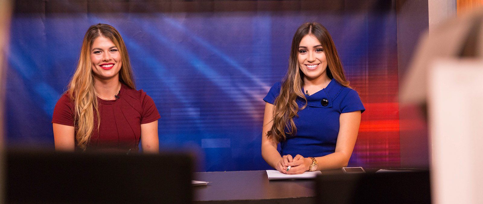 Two female students tv hosts smile as the camera begins recording.