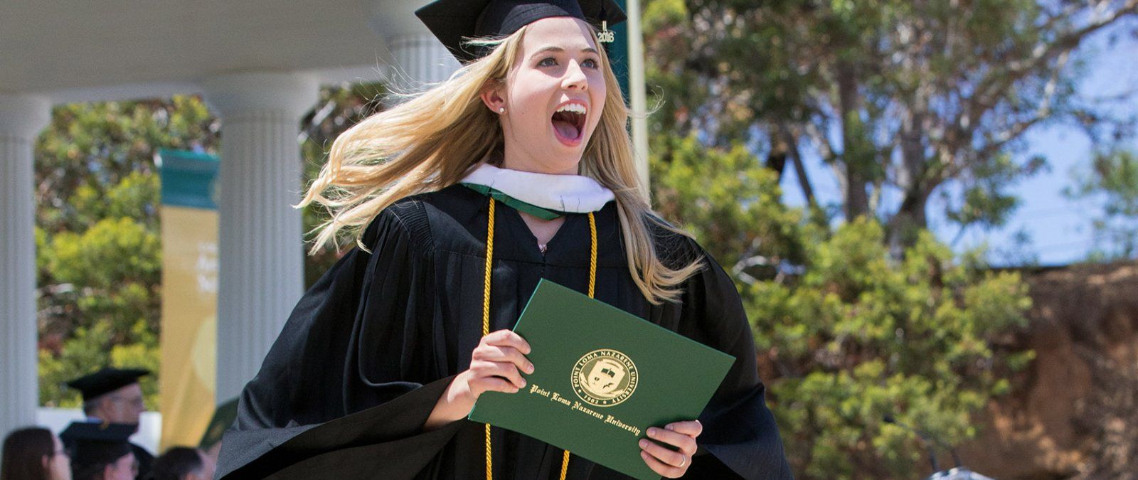 A female PLNU student excitedly smiles to the crowd after receiving her diploma. 