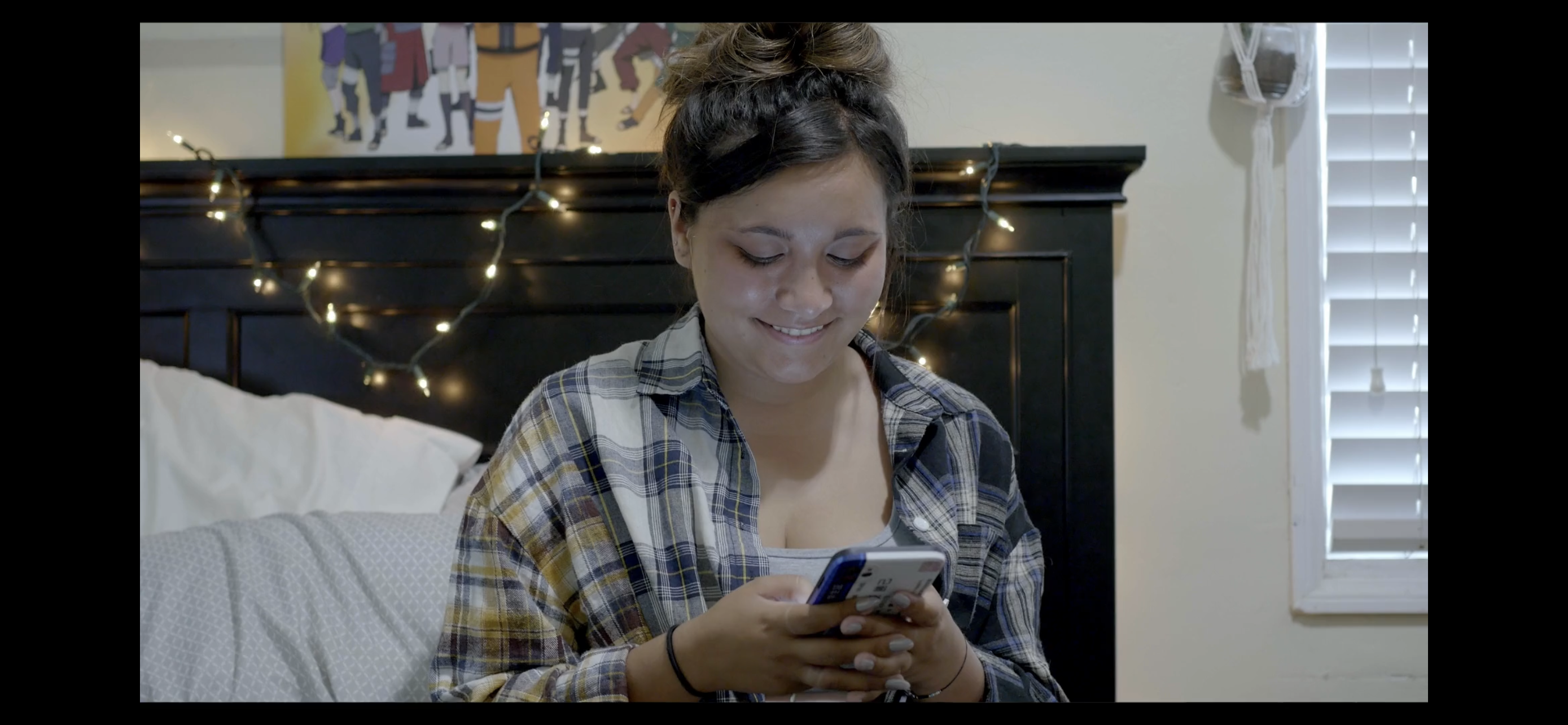 Teenage girl sits on bed while texting on her cell phone