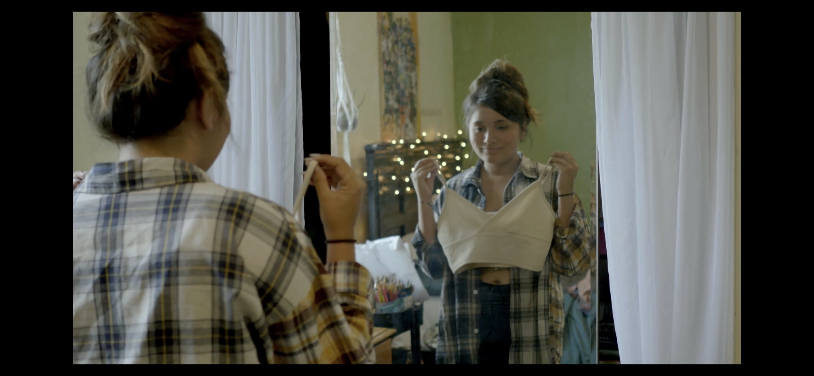 Teenage girl holds up top in front of mirror