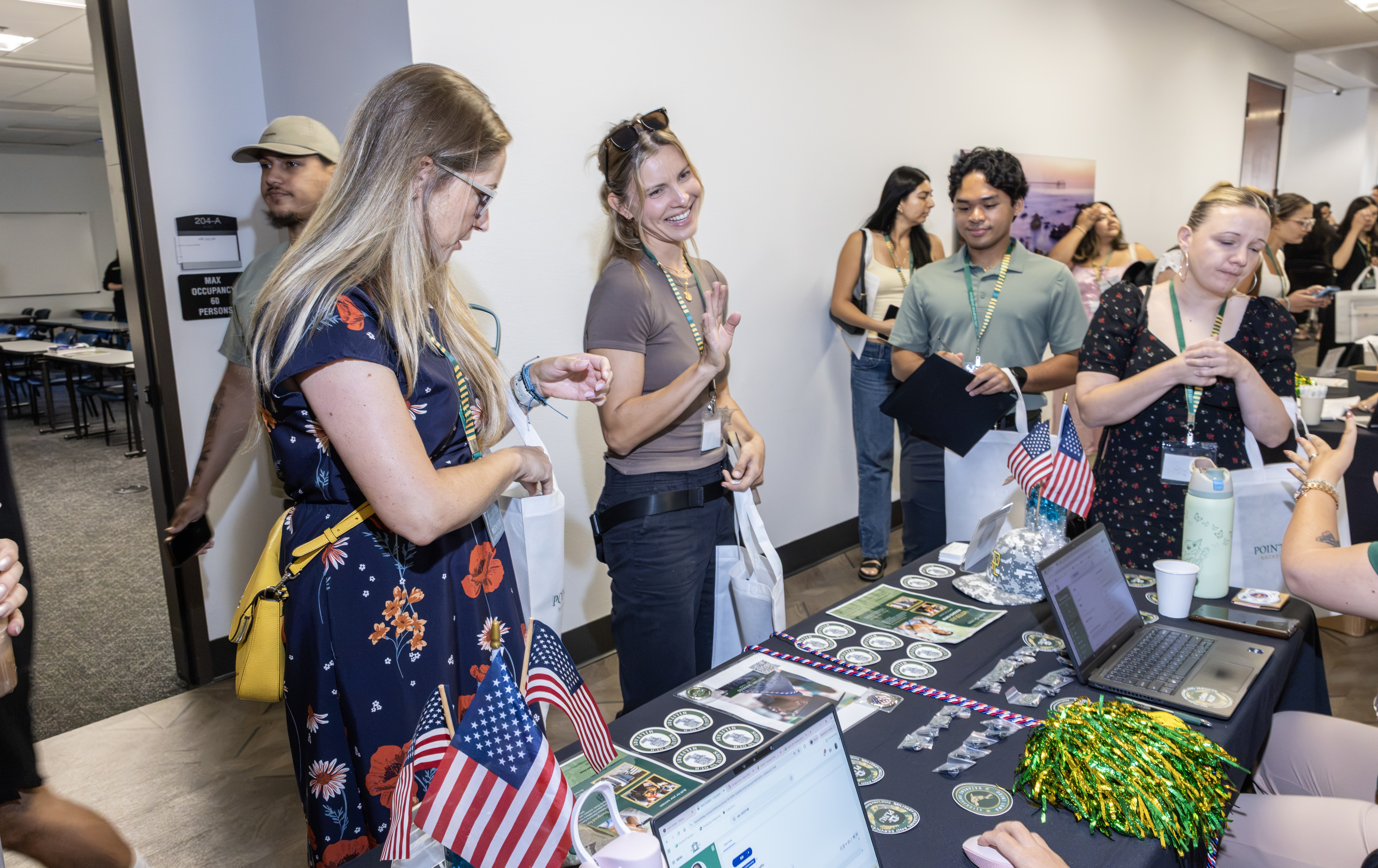 PLNU community members gathering around a resource table with informational materials and American flags.