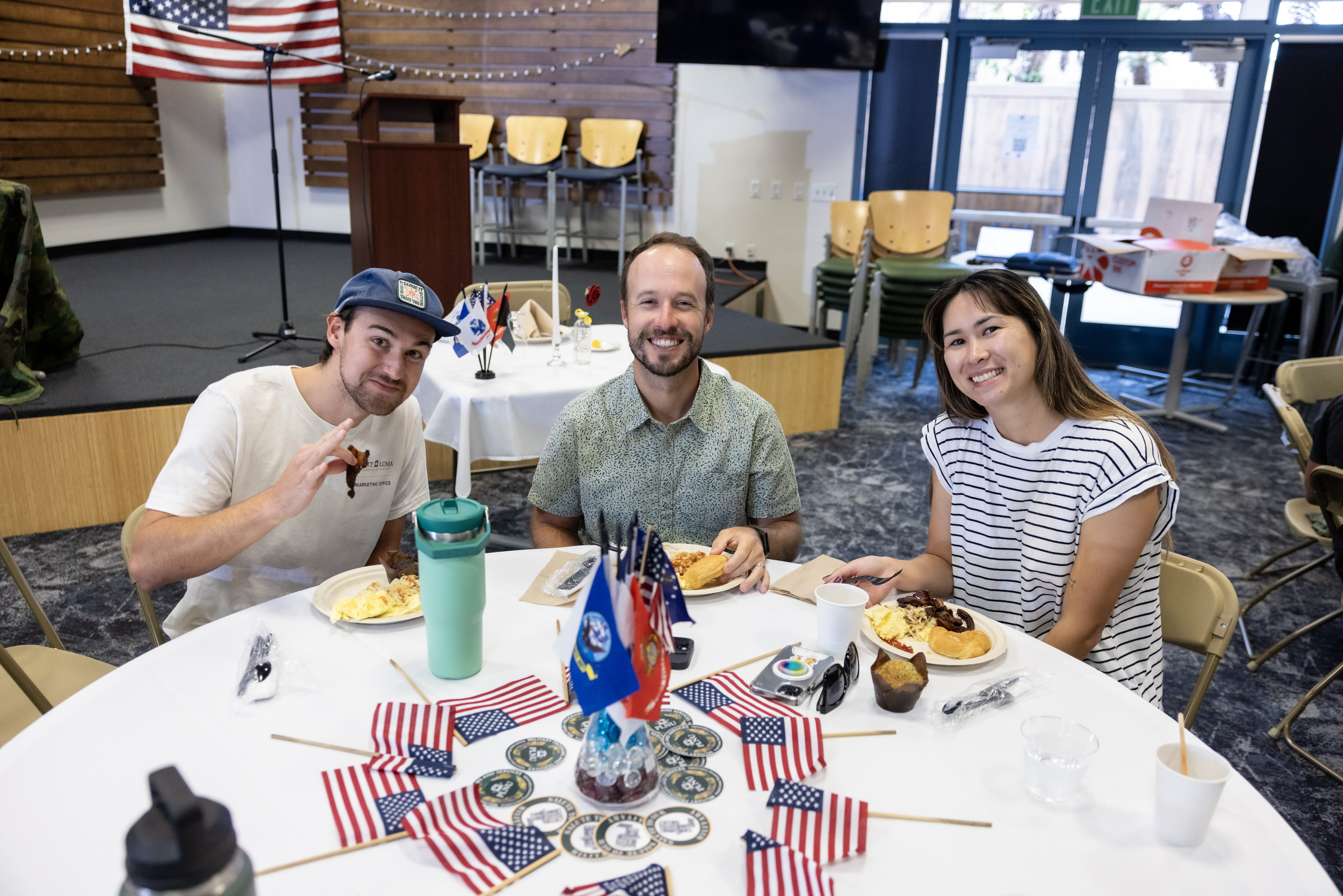 Three members of the PLNU community gather around a table decorated with American and military service flags.