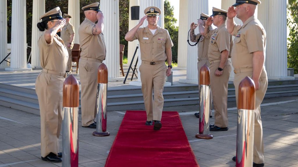 Uniformed military service members salute to one another at the Commissioning Ceremony held at the Greek.