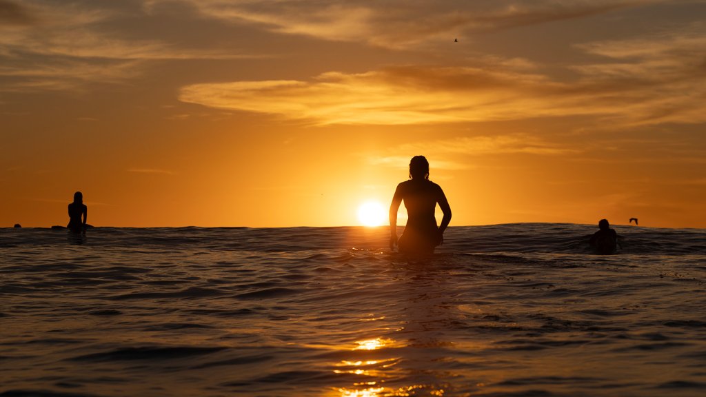 Sunset along the Pacific Ocean with surfers in the water watching.