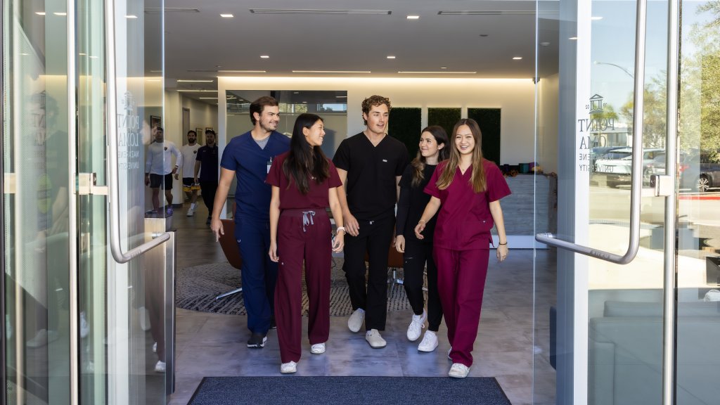 PLNU nursing students dressed in scrubs connecting in conversation while walking through entrance doors of Balboa Campus.