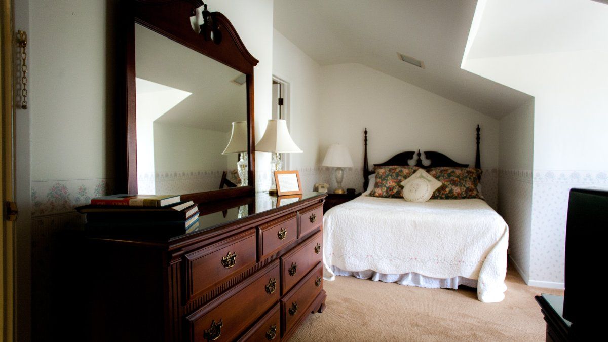 A small bedroom with a queen sized bed and a large wooden dresser