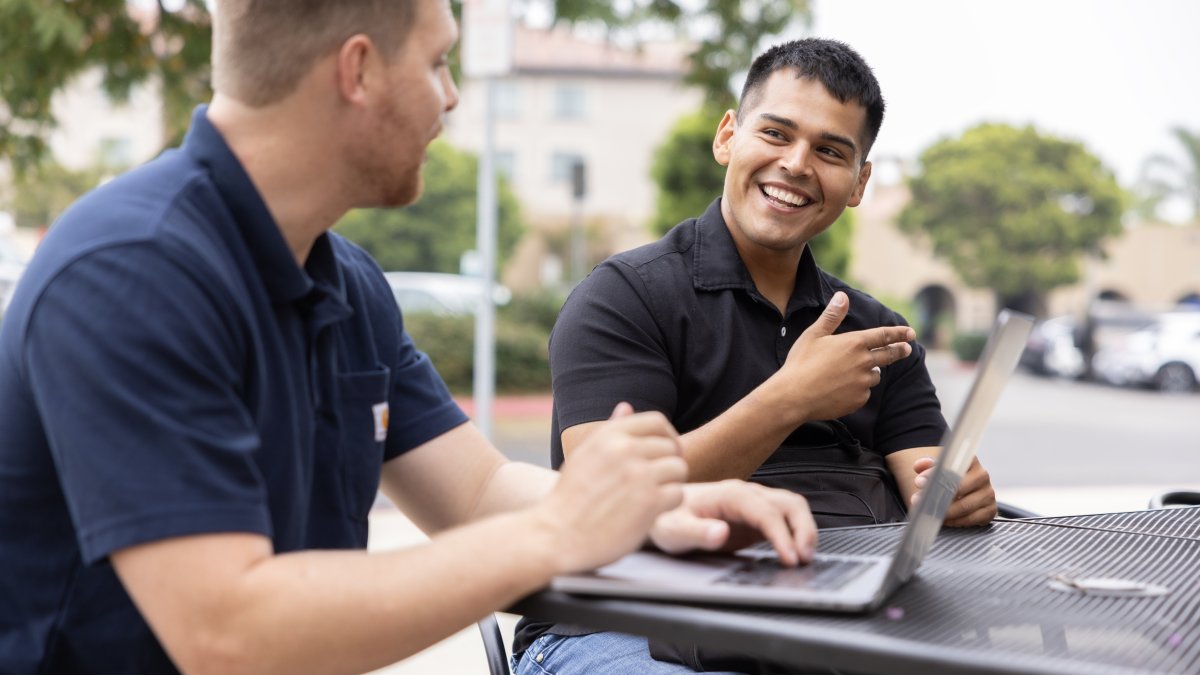 Two PLNU students work on laptops outside 