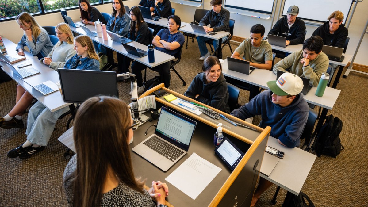 Students working on a project with the direction of a Professor. Laptops are open and students are collaborating with each other. 