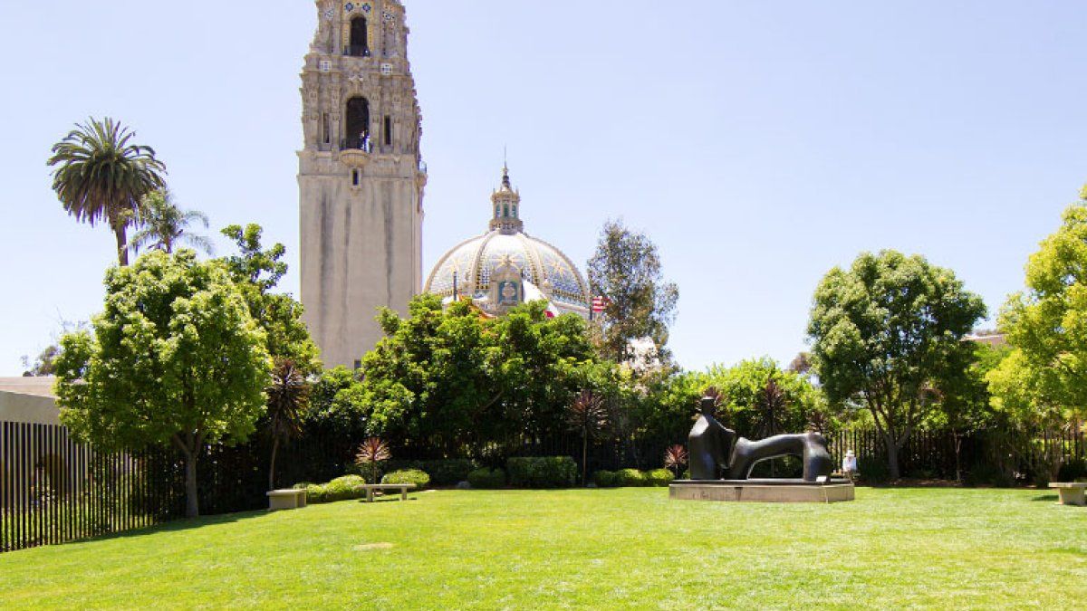 The California tower and dome rise above a grassy lawn in Balboa Park on a sunny day