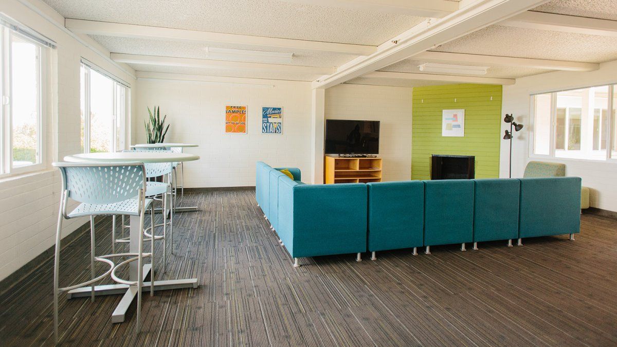 The green and teal lounge space of Finch Hall with TV, couches, and smaller tables. 