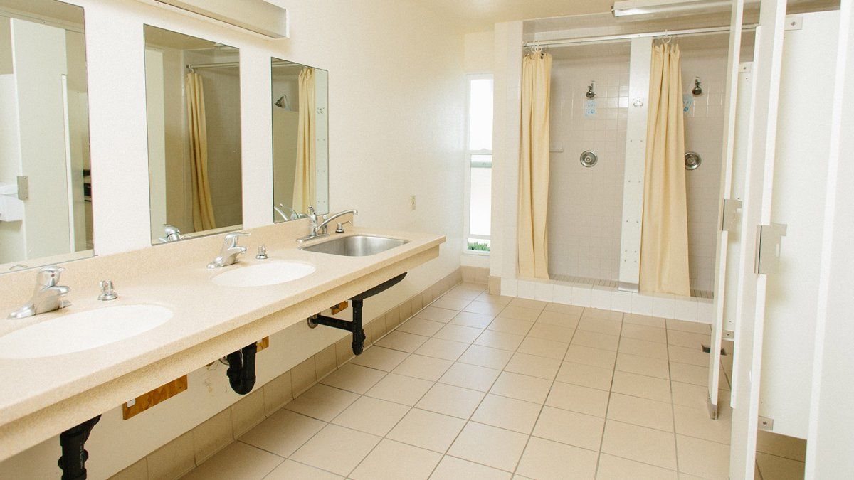 Large bathroom space with multiple shower stalls, sinks, and toilets.