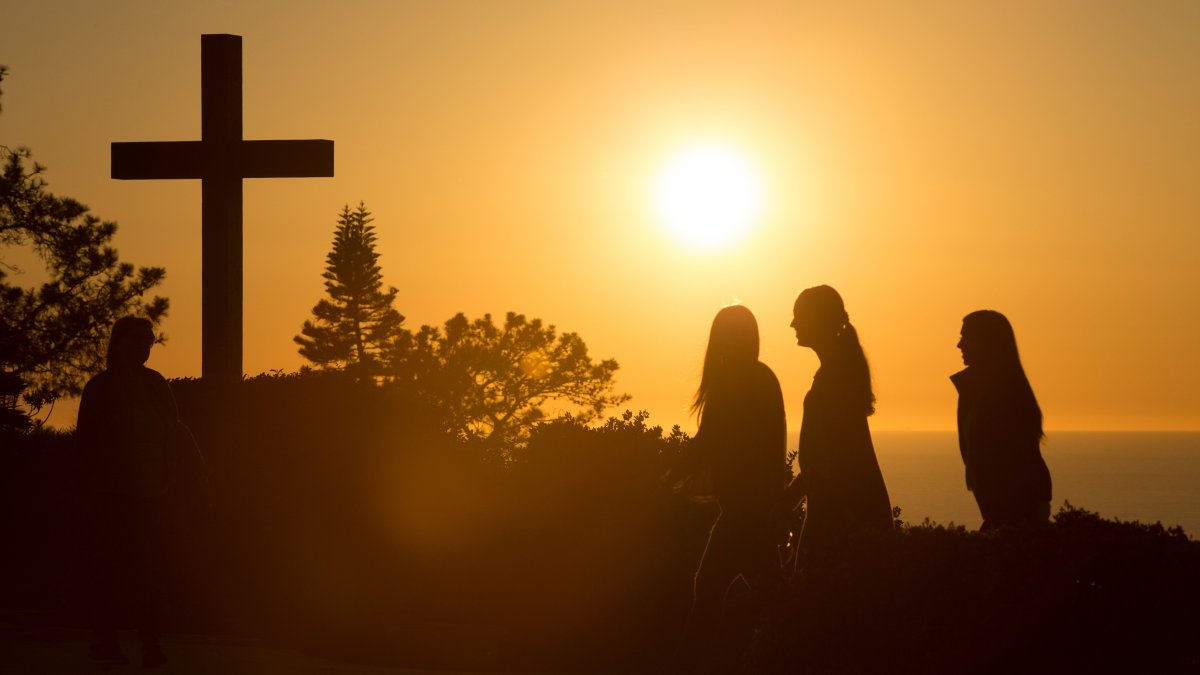 Students walk past the cross on PLNU campus during sunset