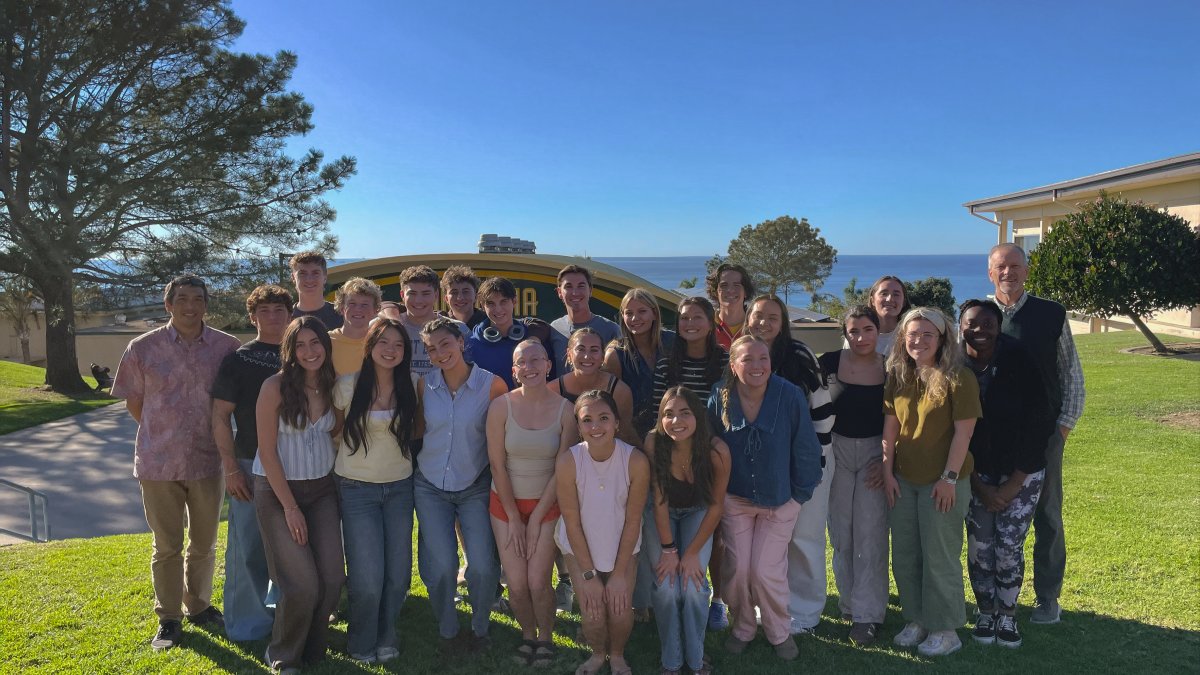 PLNU honors program students pose for a photo outside in front of the Gold Gymnasium with the Pacific Ocean in the background.