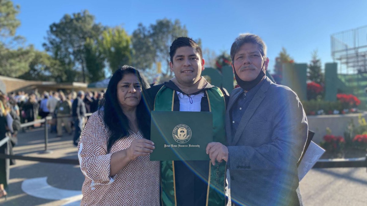 Erick is posing after graduation holding up his diploma with his parents to his left and right. 