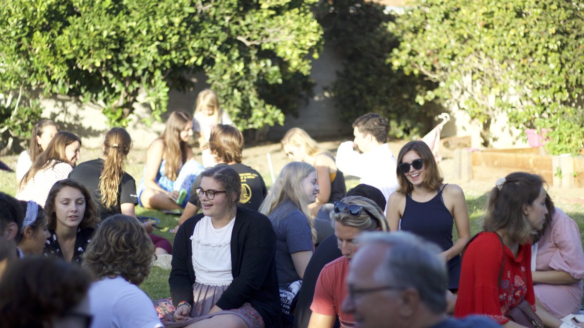 PLNU students sit outside together on a lawn socializing.