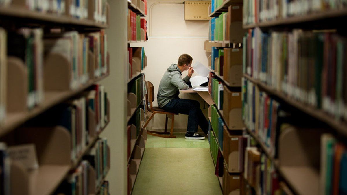 A student looks at his notes and studies on the lower floor of Ryan Library near the bookshelves.