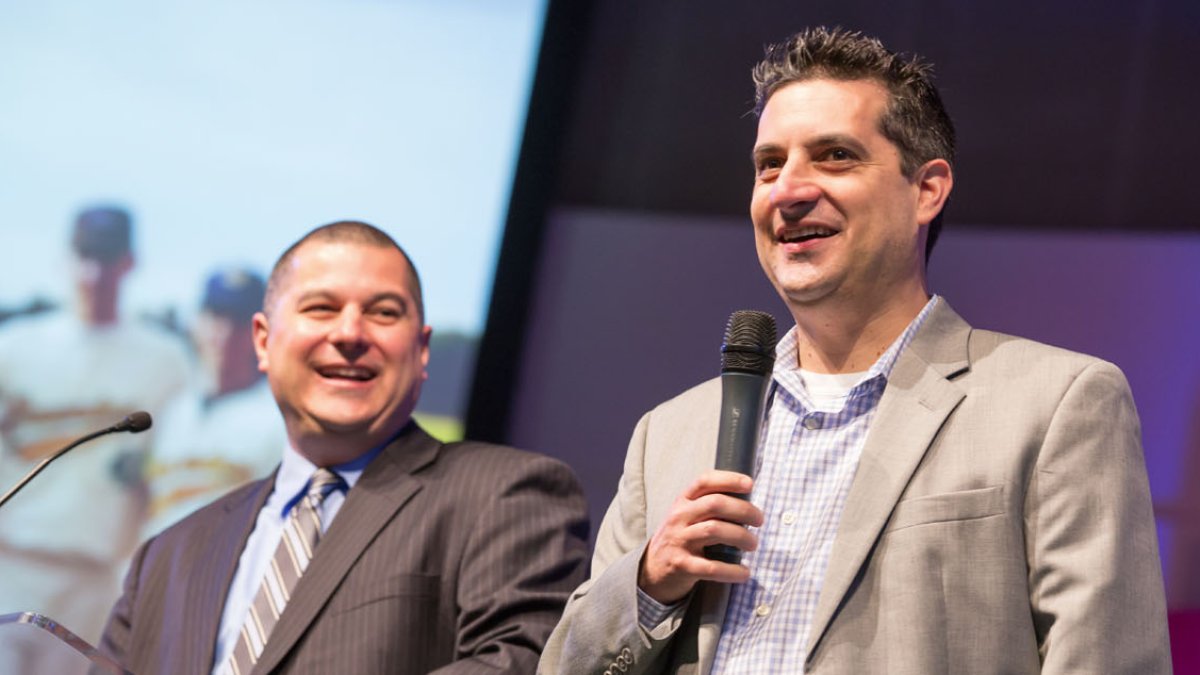 Dan and Damen Lopez stand on stage in suits holding microphones