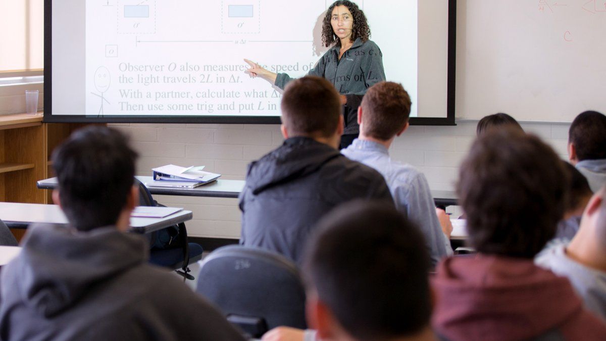 A professor teaches her class using a projector screen.
