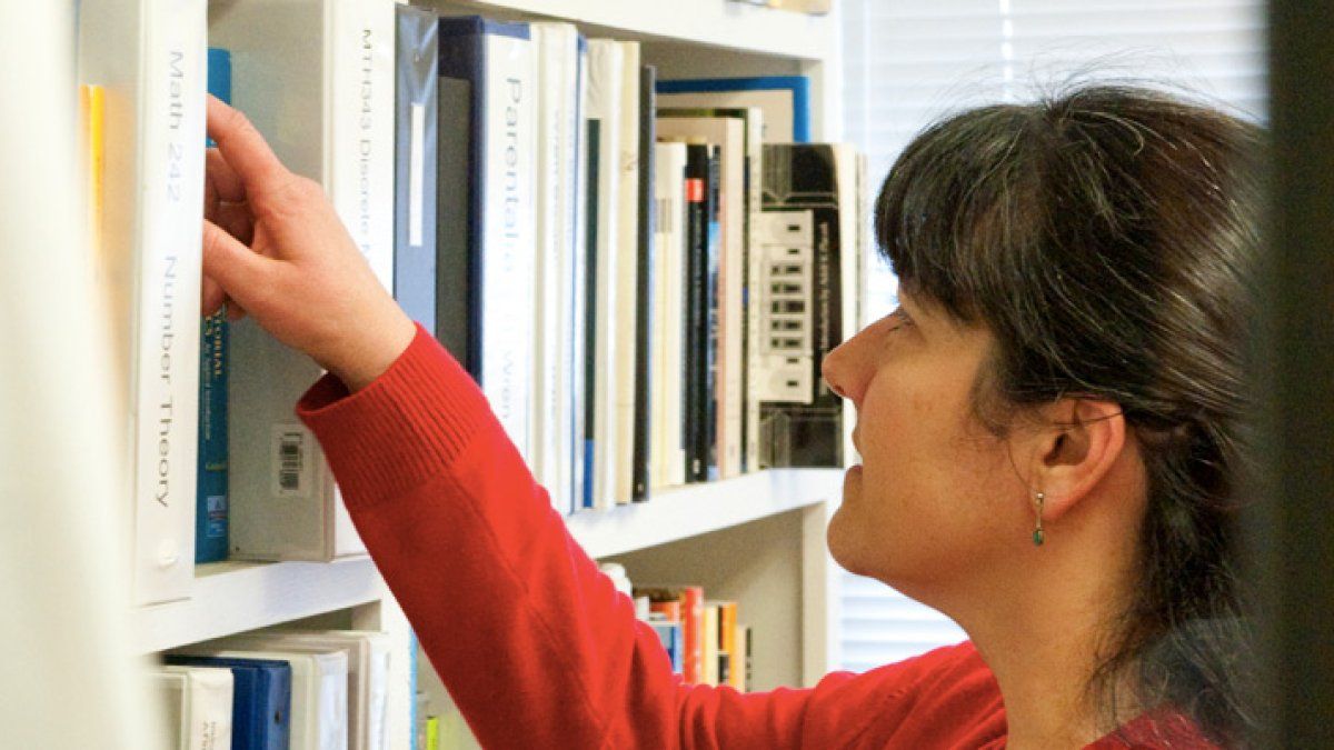 Maria Zack reaches for a book in her office bookcase.