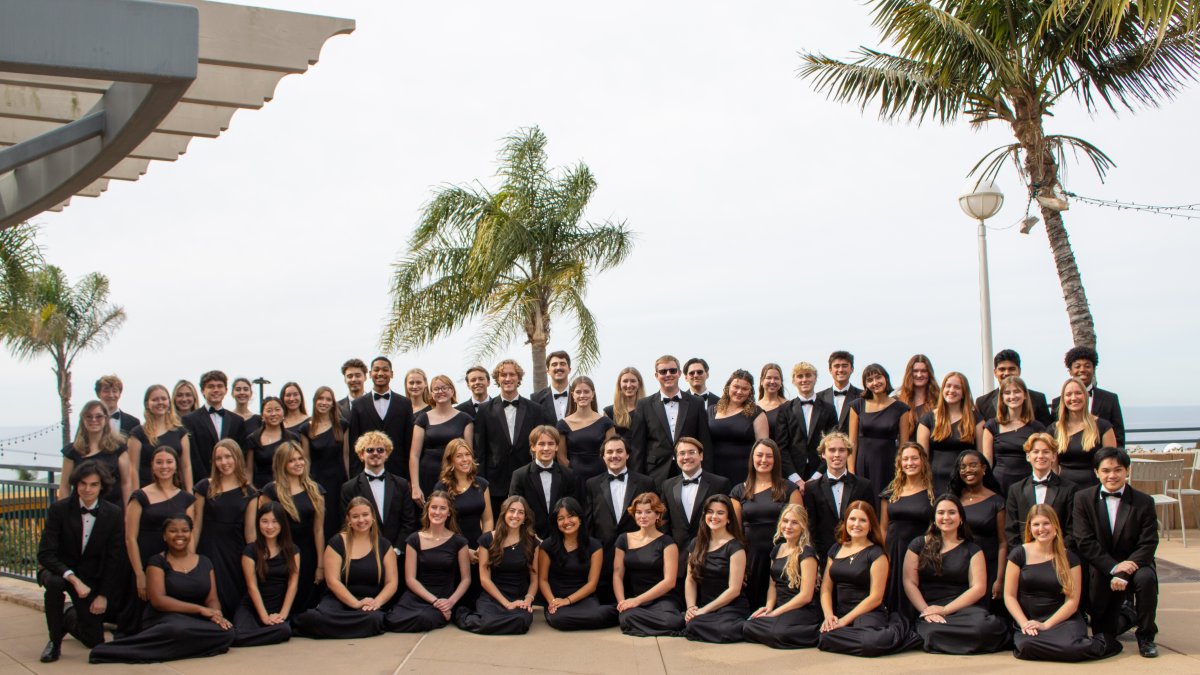 Students in the PLNU choir gather for a group photo on campus with ocean views in the background.