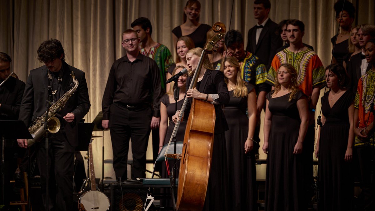 PLNU music students perform on stage during an ensemble concert featuring vocalists and instrumentalists.