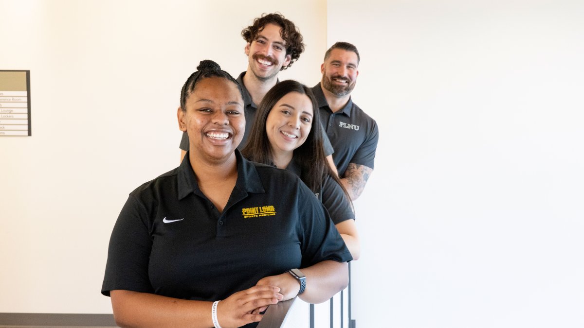 Four students smiling for a photo while leaning on a railing 