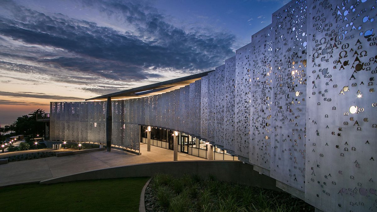 The alpha and omega metal pane wall sloping outward toward the twilight sky