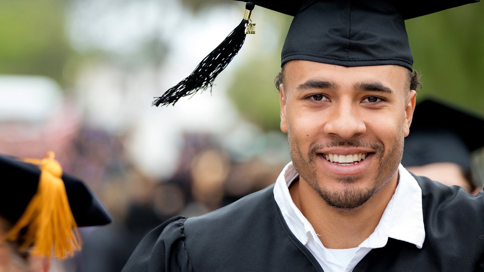 A PLNU student smiles as he stands to receive his diploma at commencement.
