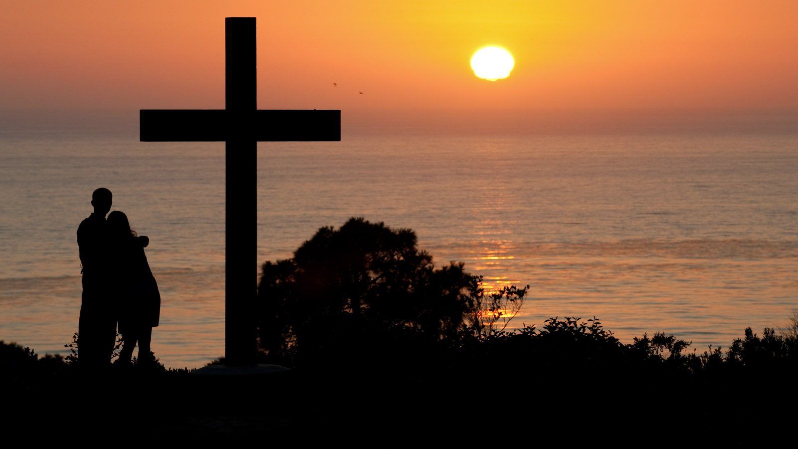 Two students watch the sunset over the Pacific Ocean from the cross on PLNU's campus