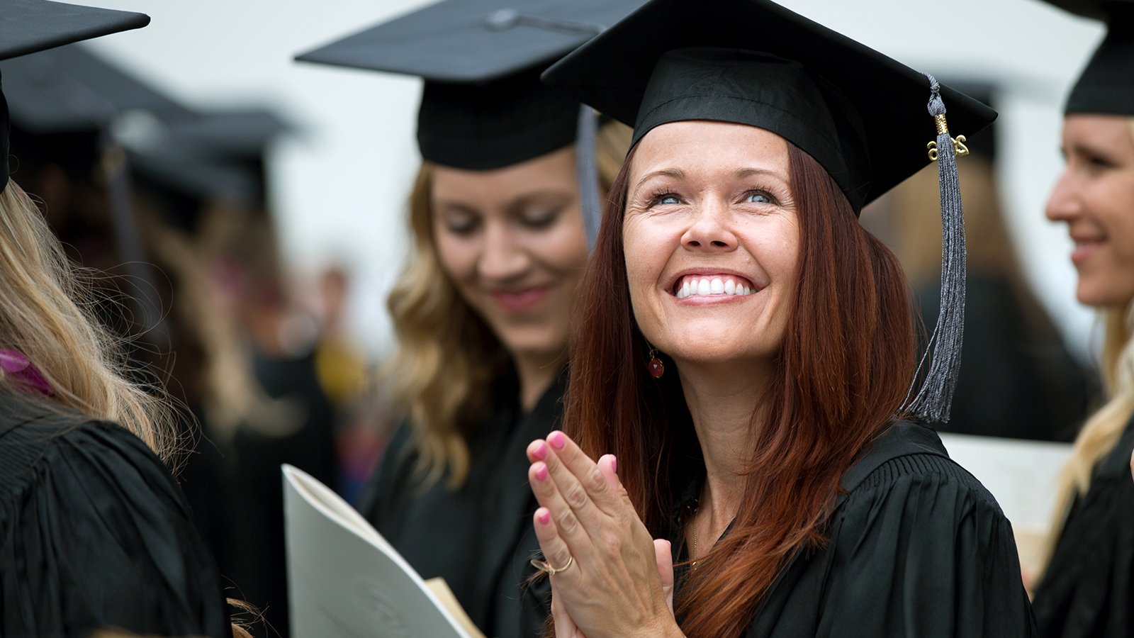 A female graduate student smiles up at her friends and family during commencement.