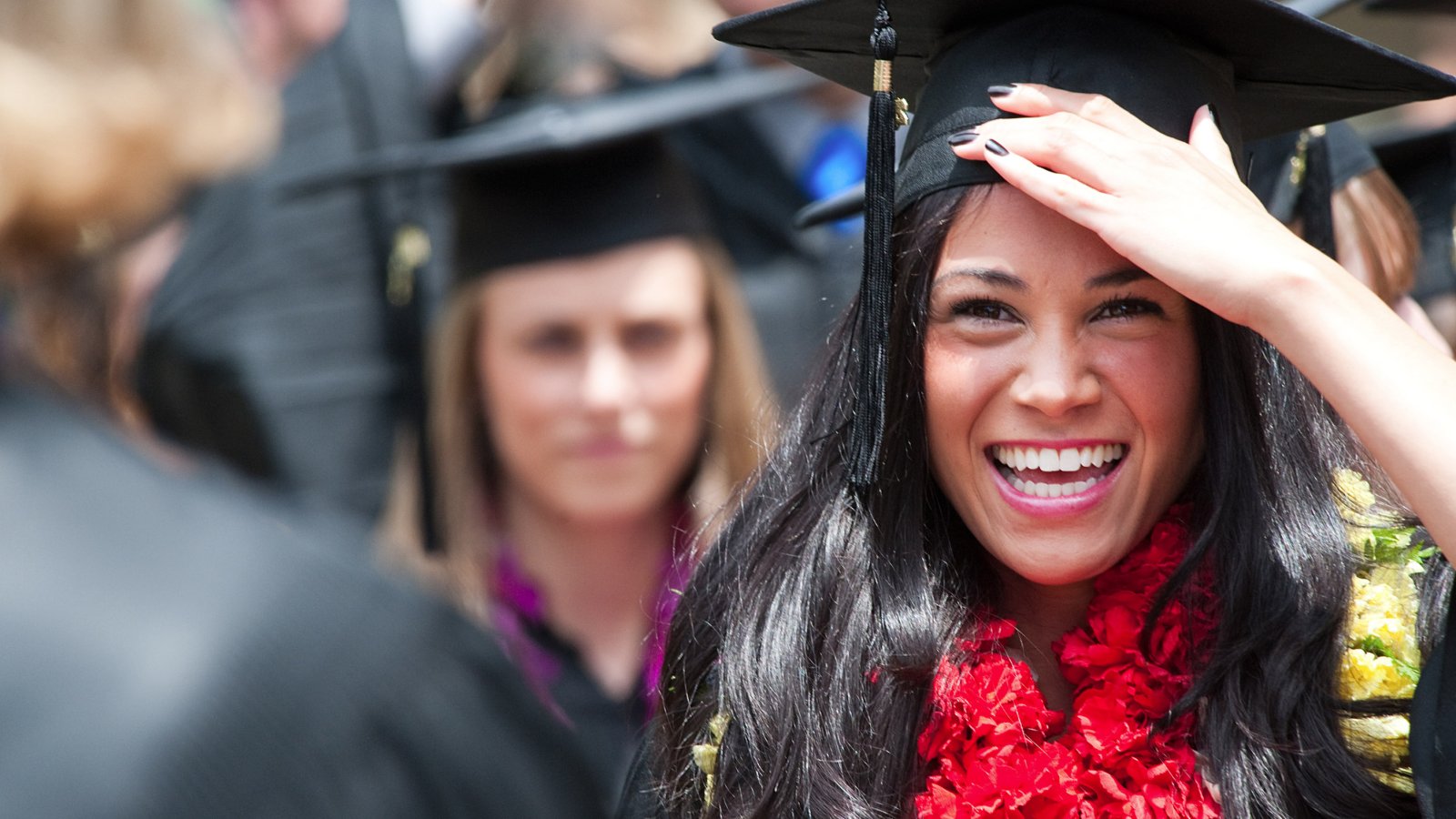 Female student stands out of a crowd at graduation as she holds her cap and smiles in celebration