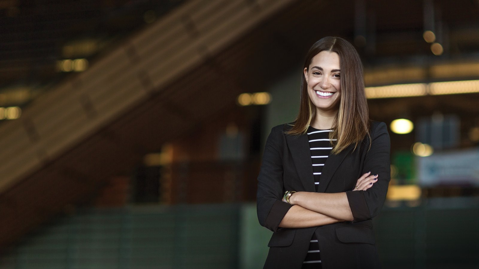A PLNU alumni stands with her arms crossed and confidently smiles to the camera in downtown San Diego.