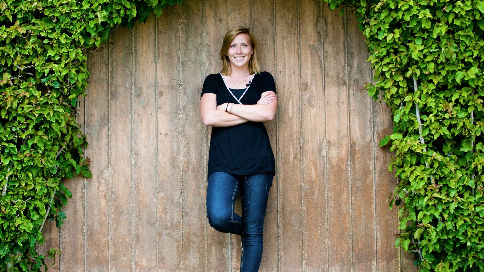 Student leans confidently on an ivy-covered wall on campus