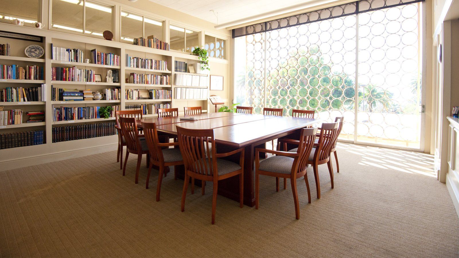 Conference Room with empty square table with a wall of books behind and a wall of windows