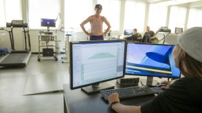 A grad student in PLNU's Integrative Wellness program sits behind a computer monitor. The monitor is displaying charts that recorded the movement of another female student who is standing in front of her.