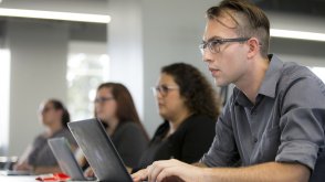 PLNU student typing notes on laptop during class lecture.