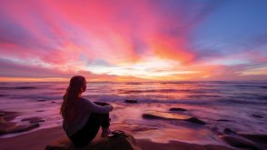 Woman sits on the beach during sunset