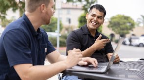 Two PLNU students work on laptops outside 