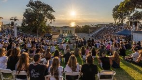Image of PLNU community sitting and facing sunset along Pacific Ocean at the Greek Amphitheater for Welcome Week event.