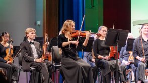 female student playing violin amongst orchestra