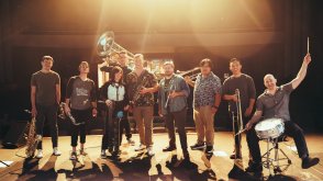 9 muscians on a performance stage holding various brass and percussion instruments