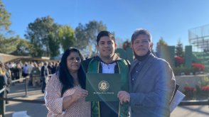 Erick is posing after graduation holding up his diploma with his parents to his left and right. 