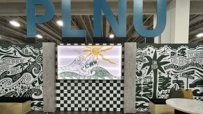 PLNU's vendor set up at the Nazarene Youth Center Conference in 2026 with the university's logo sitting above the set up with Loma graphics along the wall and a seating area for visitors.