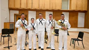 five brass musicians in navy band uniform holding their instruments