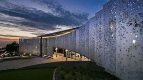 The alpha and omega metal pane wall sloping outward toward the twilight sky