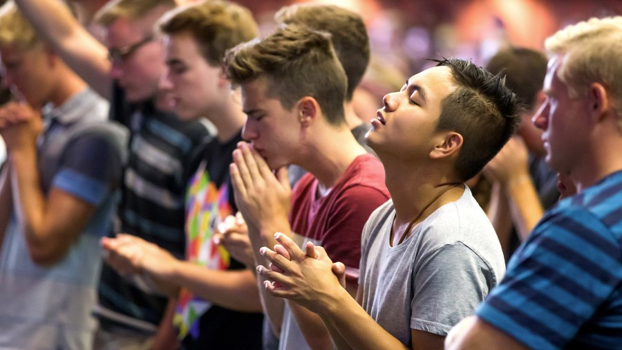 Group of young men praying and worshiping in brown chapel